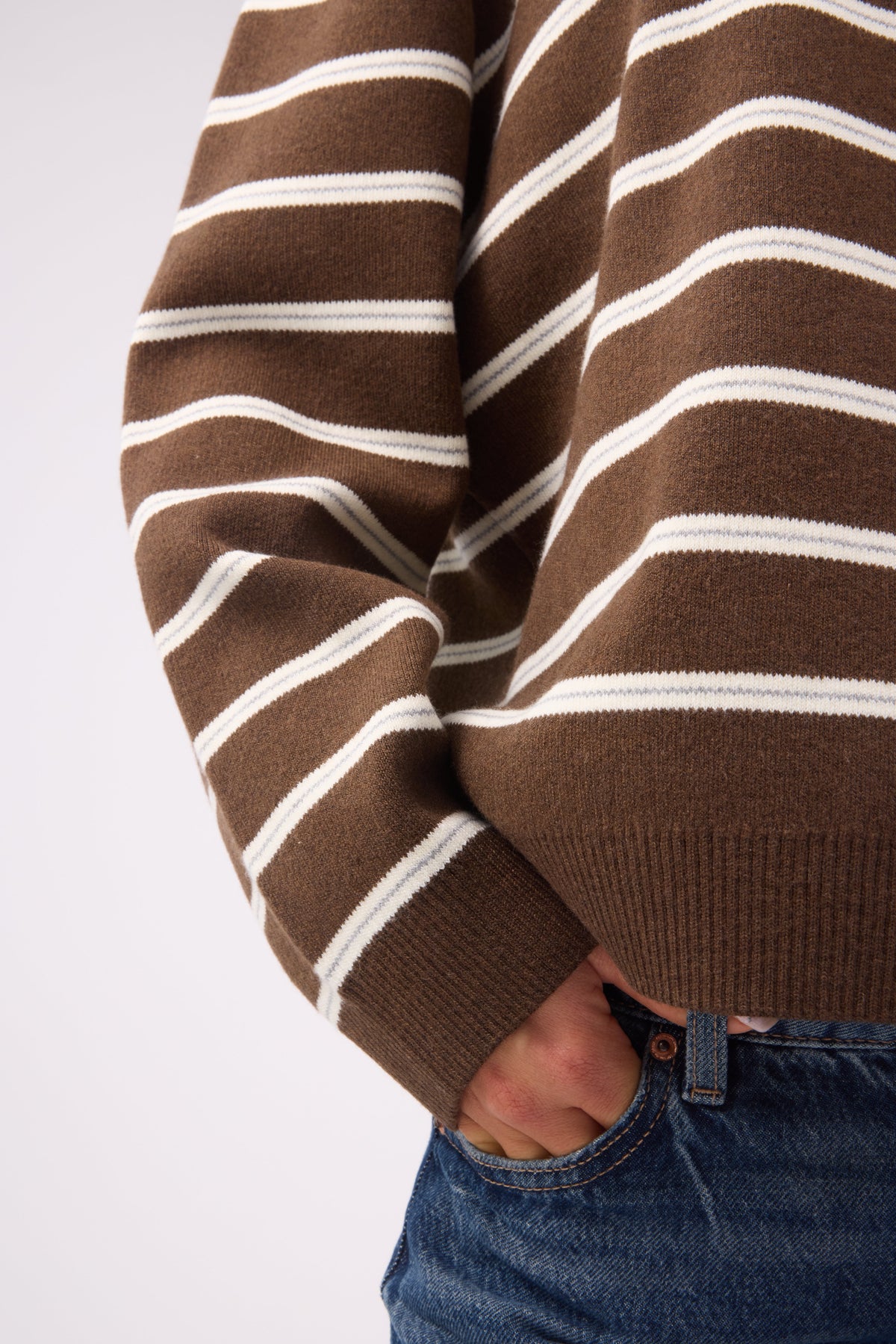 A close up view of a youg woman wearing a brown & cream stripe swater with a ribbed waist and rivbbed cuffs.