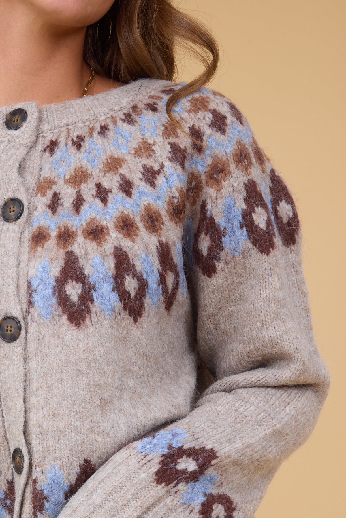 A close up view of a woman wearing buton down cardigan witha blue & brown nordic pattern.