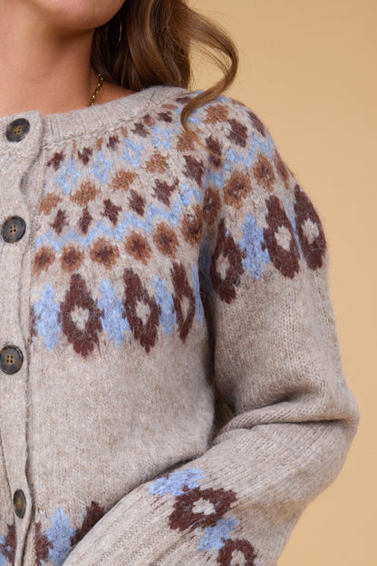 A close up view of a woman wearing buton down cardigan witha blue & brown nordic pattern.