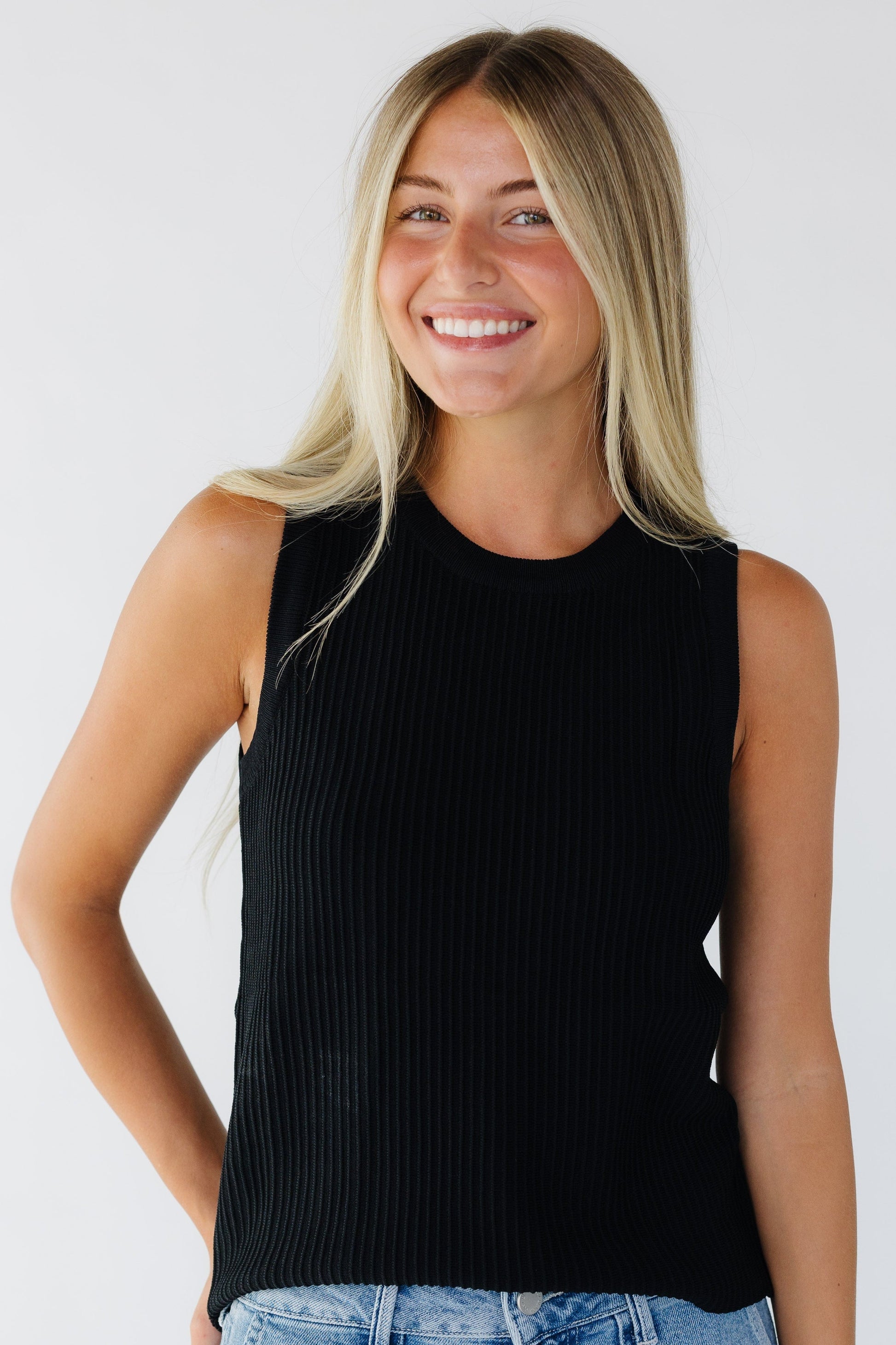 Young woman wearing a black tank top with a ridge texture and a round neckline.
