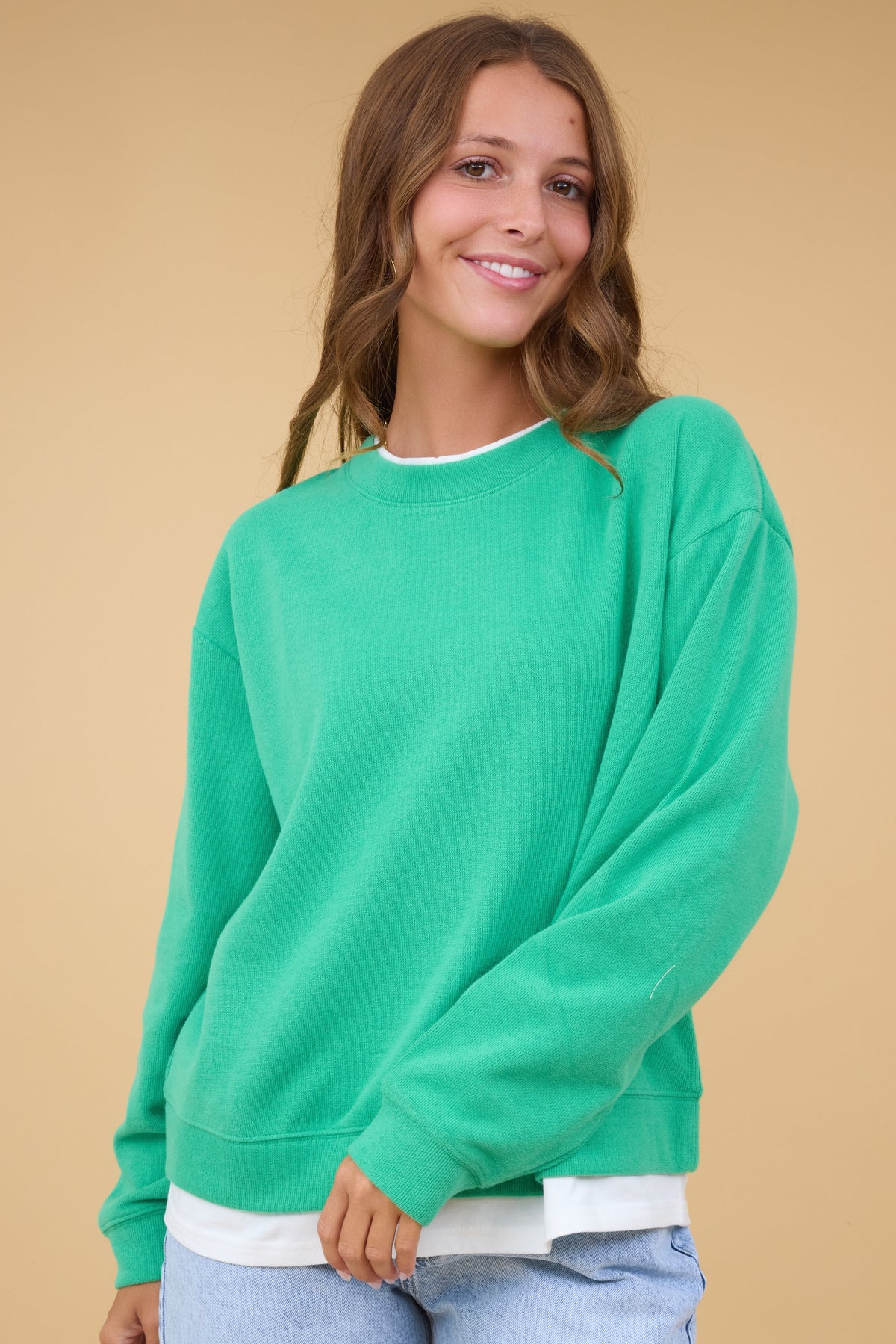 Woman wearing a green loose fitting sweatshirt with faux white undertee details.