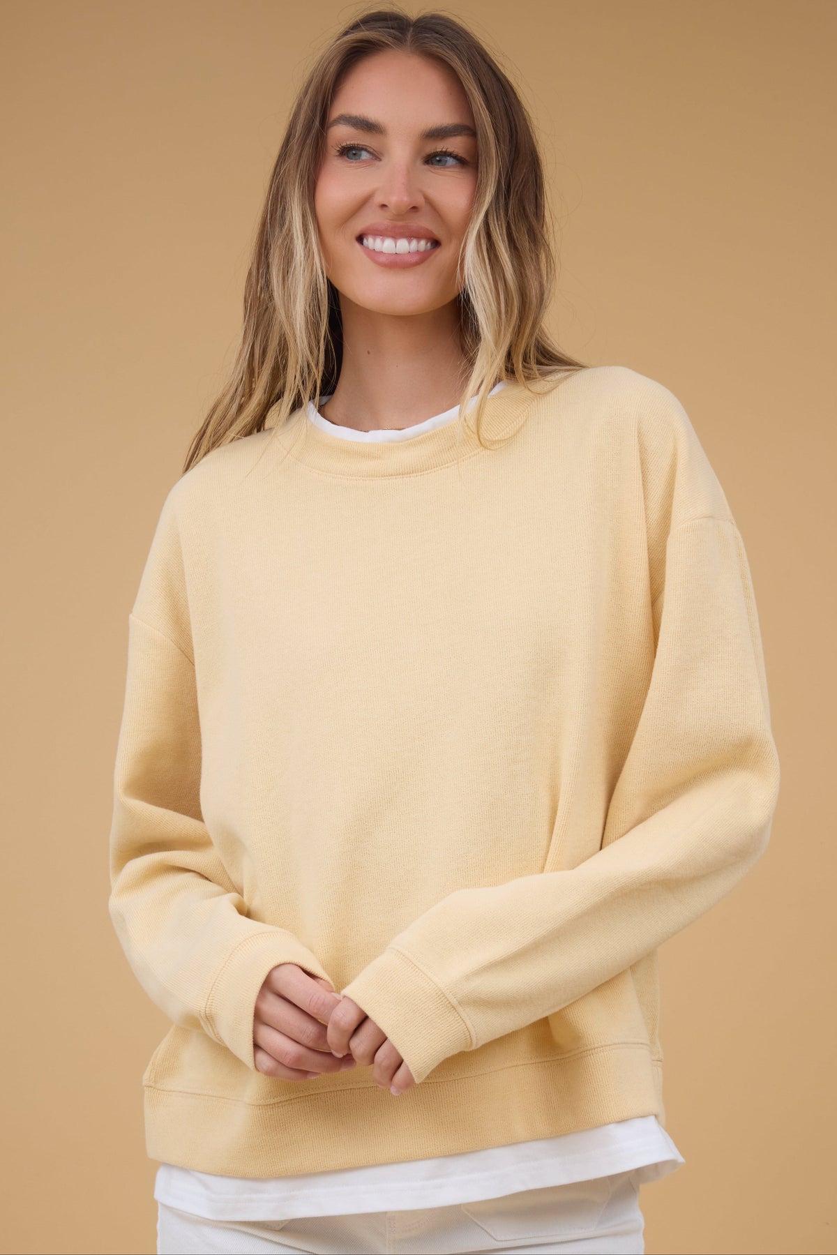 Young woman wearing a yellow sweatshirt with additionl details that look like a white tee at the collar & the hem.