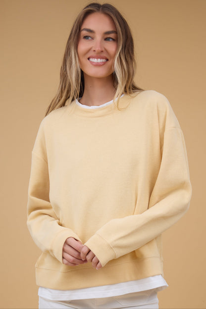 Young woman wearing a yellow sweatshirt with additionl details that look like a white tee at the collar & the hem.