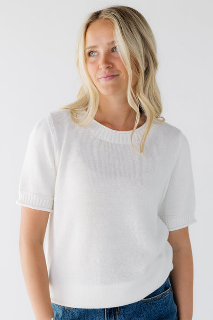 Young woman wearing an off white pullover sweater with short sleeves.