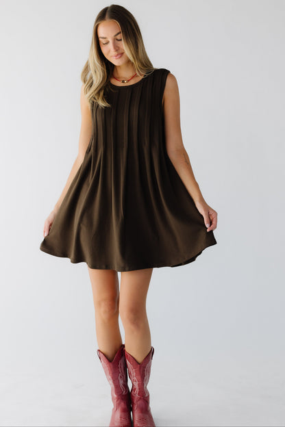 Young woman wearing a  brown short sleeveless mini dress with front pleats and a round necklinel.