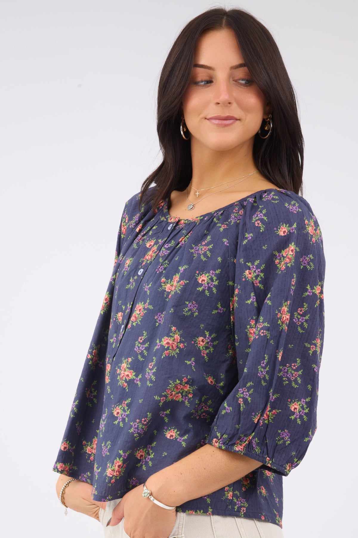A young woman wearing a modest blue floral print buttonn down blouse with elbow length sleeves and a wide scoop neckline.