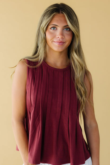 Young woman wearing a wine color sleeveless bloues with front pleats and a round neckline.