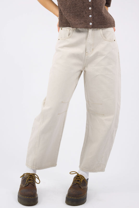 A young woman wearing a modest pair of ecru, wide leg barrel jeans with darts at the knee, 5 pockets and a zipper-button closure.