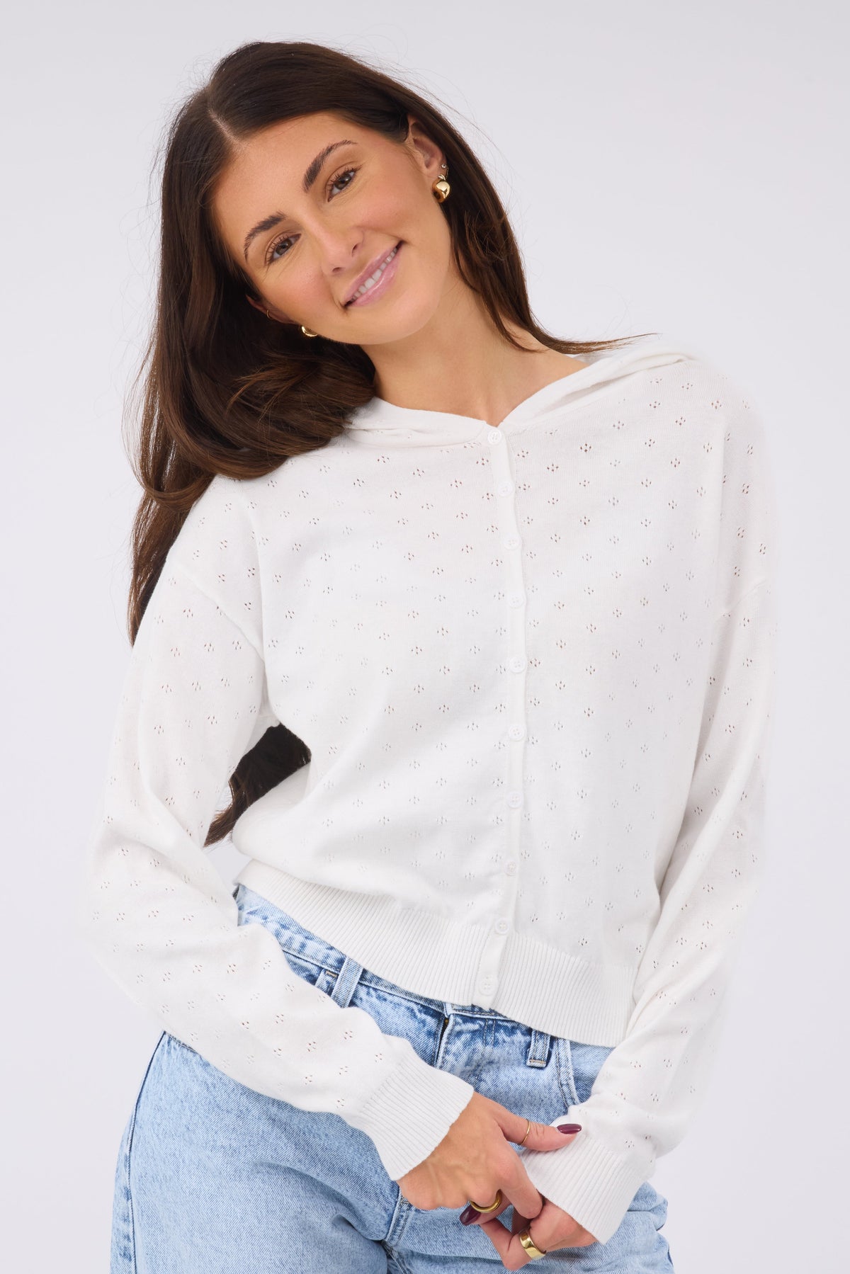 A woman wearing a white long sleeve, button down cardigan in a white pointelle knit with long sleeves.