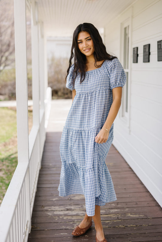 Young woman wearing a modest blue & white plaid loose fitting midi dress with a square neckline and short puff sleeves.