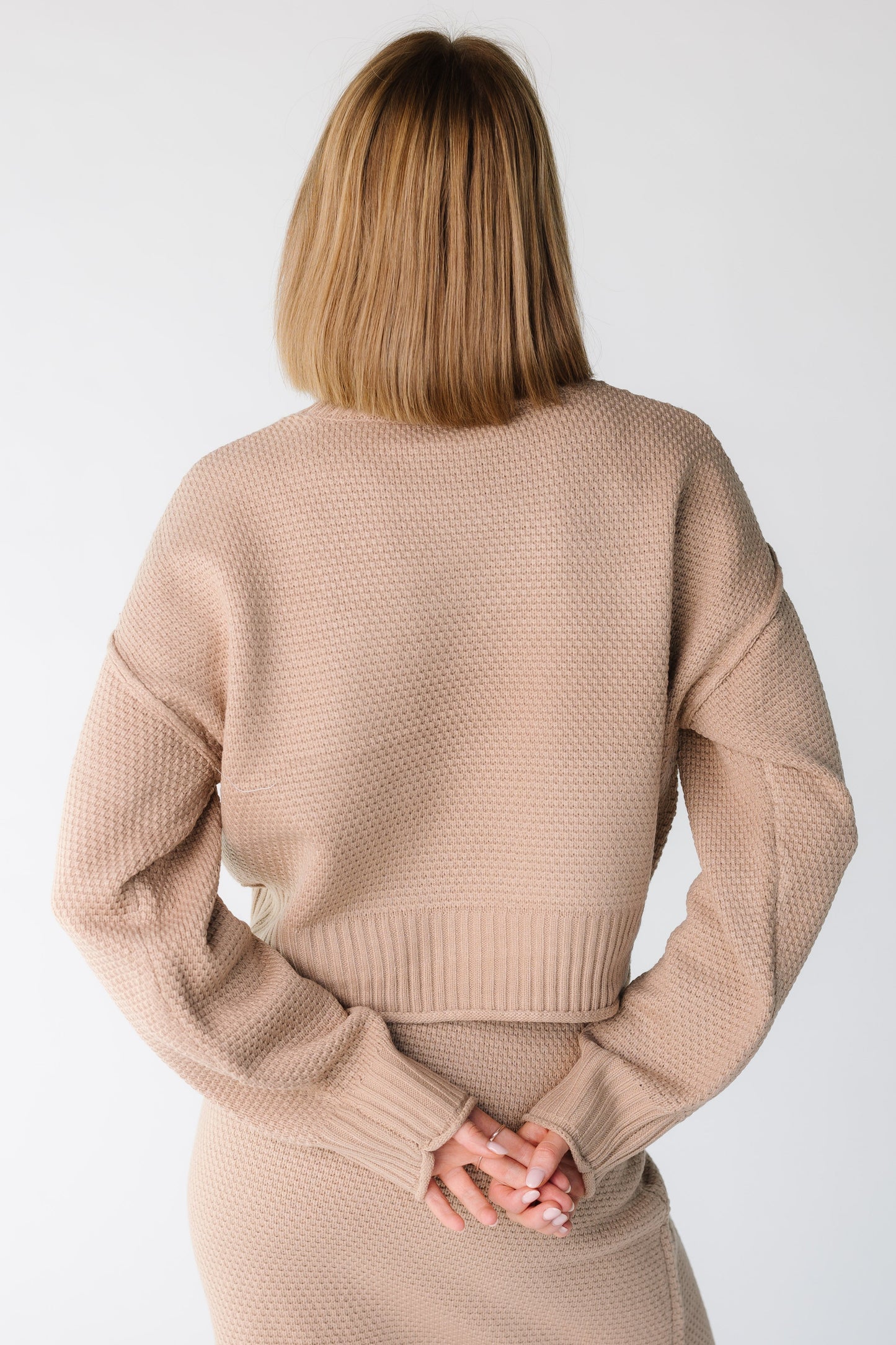 Back view of a women wearing a taupe long sleeve textured sweater