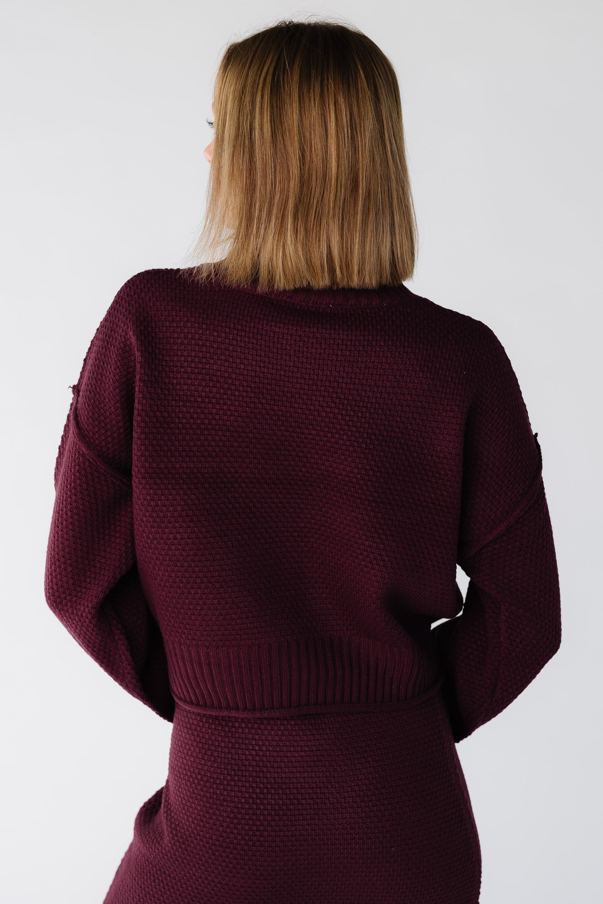 Back view of a woman wearing a long sleeve textured 2 piece sweater and skirt set