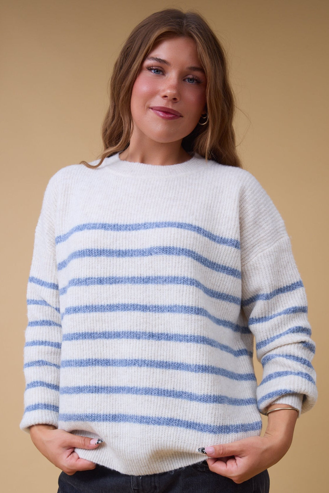 Young woman wearing a modest cream & blue stripe, rib knit sweater with long sleeves.