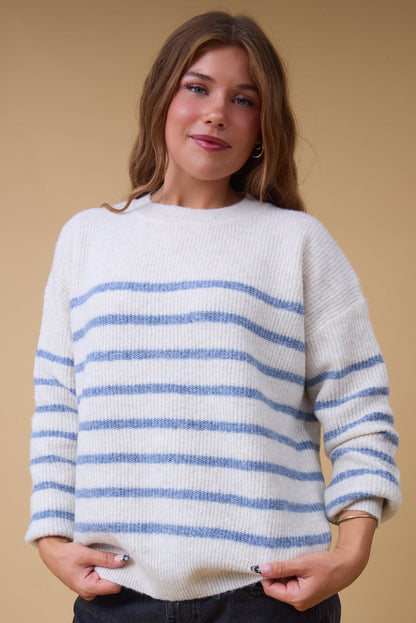 Young woman wearing a modest cream & blue stripe, rib knit sweater with long sleeves.
