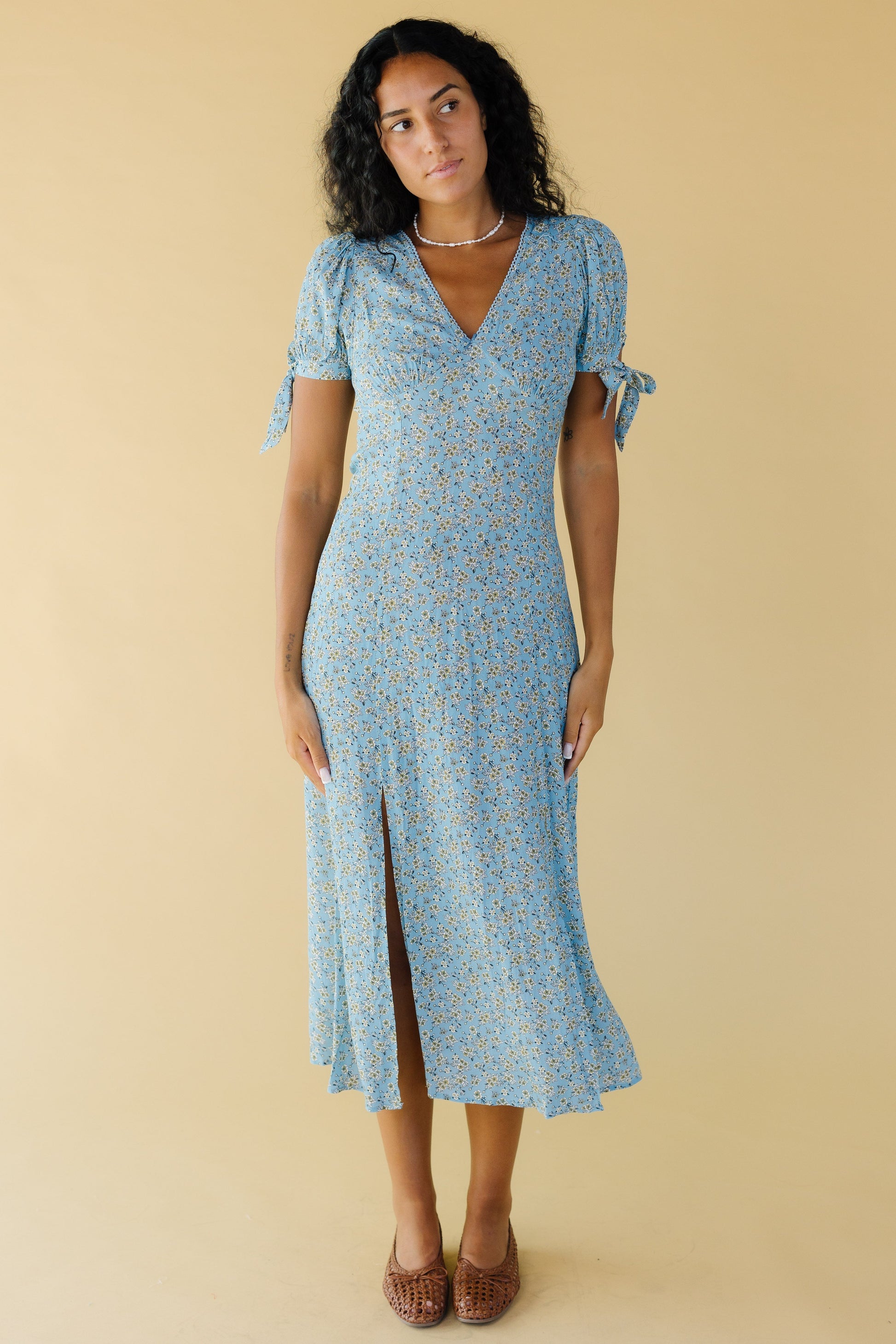 Young woman wearing a fairly close fitting light blue floral dress with a V-neckline and A-line skirt.