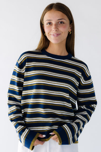 Young woman wearing a modest navy & multi color stripe loose fitting pullover sweater with a crew neckline and long loose sleeves.