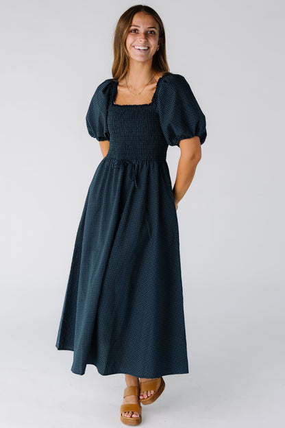 Woman wearing a navy gingham midi dress with a square neckline and smocked bodice