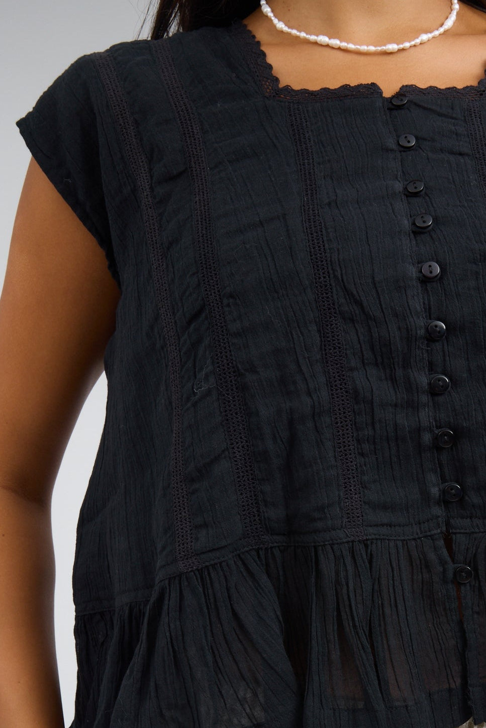 Close view of a woman wearing a loose fitting black button down blouse wth lace insets and a bottom ruffle.