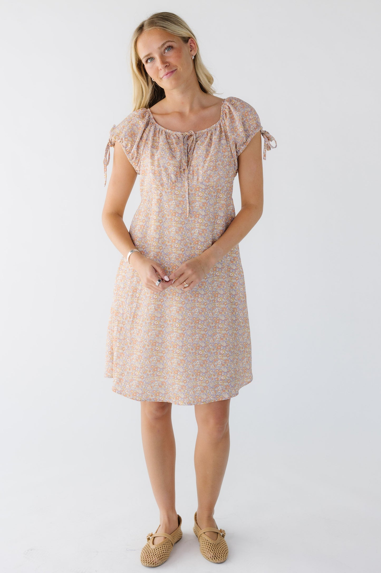 Young woman wearing a multi-color  pink knee length dress with a wide round and drawstring neckline and short puff sleeves with ties.