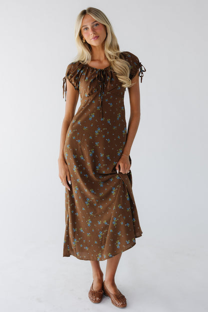 Young woman wearing a modest brown with blue floral print midi dress with a drawstring scoop neckline and puff sleeve and an empire waist.