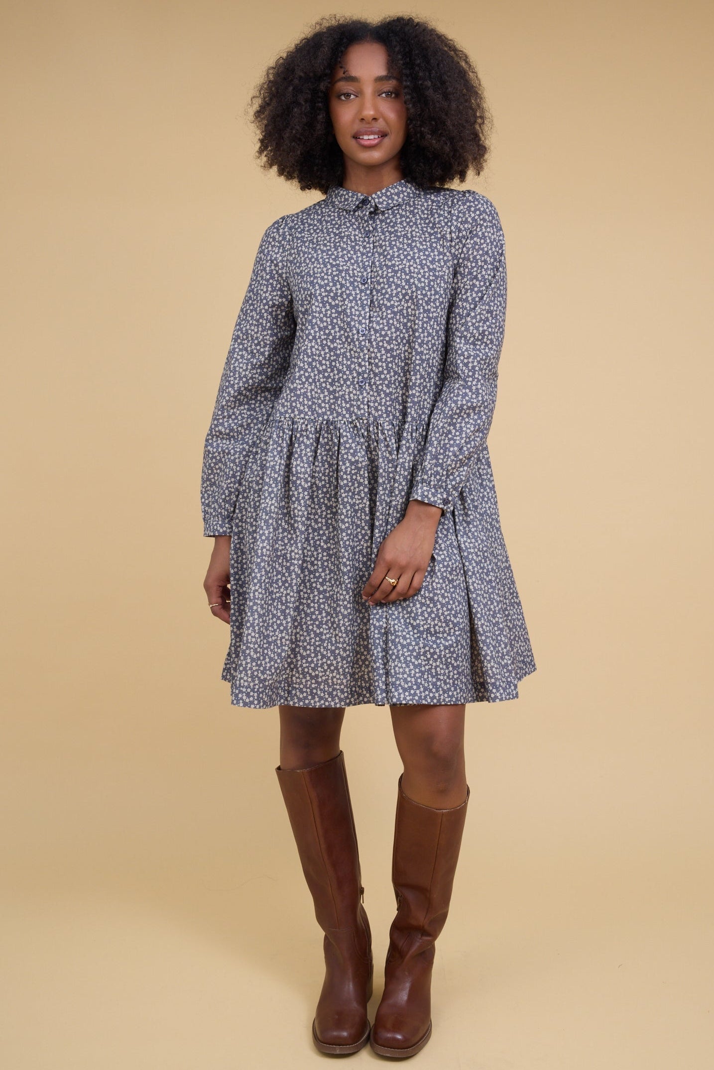 Woman wearing a modest short dress in charcoal floral print that buttons down the front to the skirt, long sleeves and a round neckline and pointed collar.