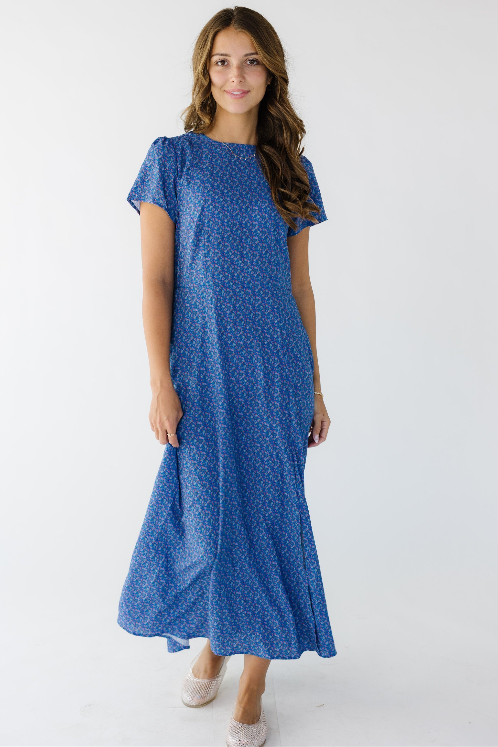 Woman wearing a blue floral sheath style midi dress with an A-line skirt and an off center front slit.