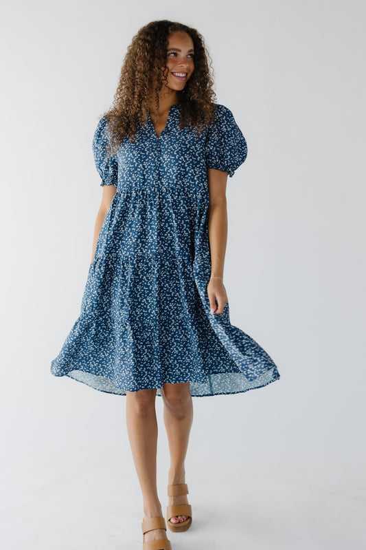 Young woman wearing a blue floral knee length dress with short puff sleeves.