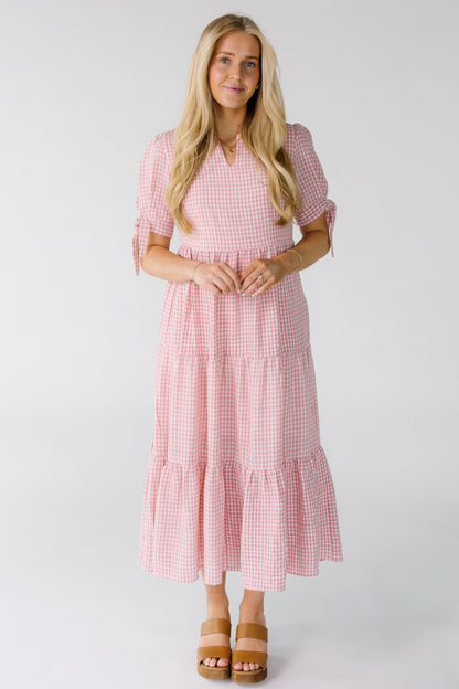 Woman wearing a pink and white gingham midi dress with tiers and short sleeves and tiers.