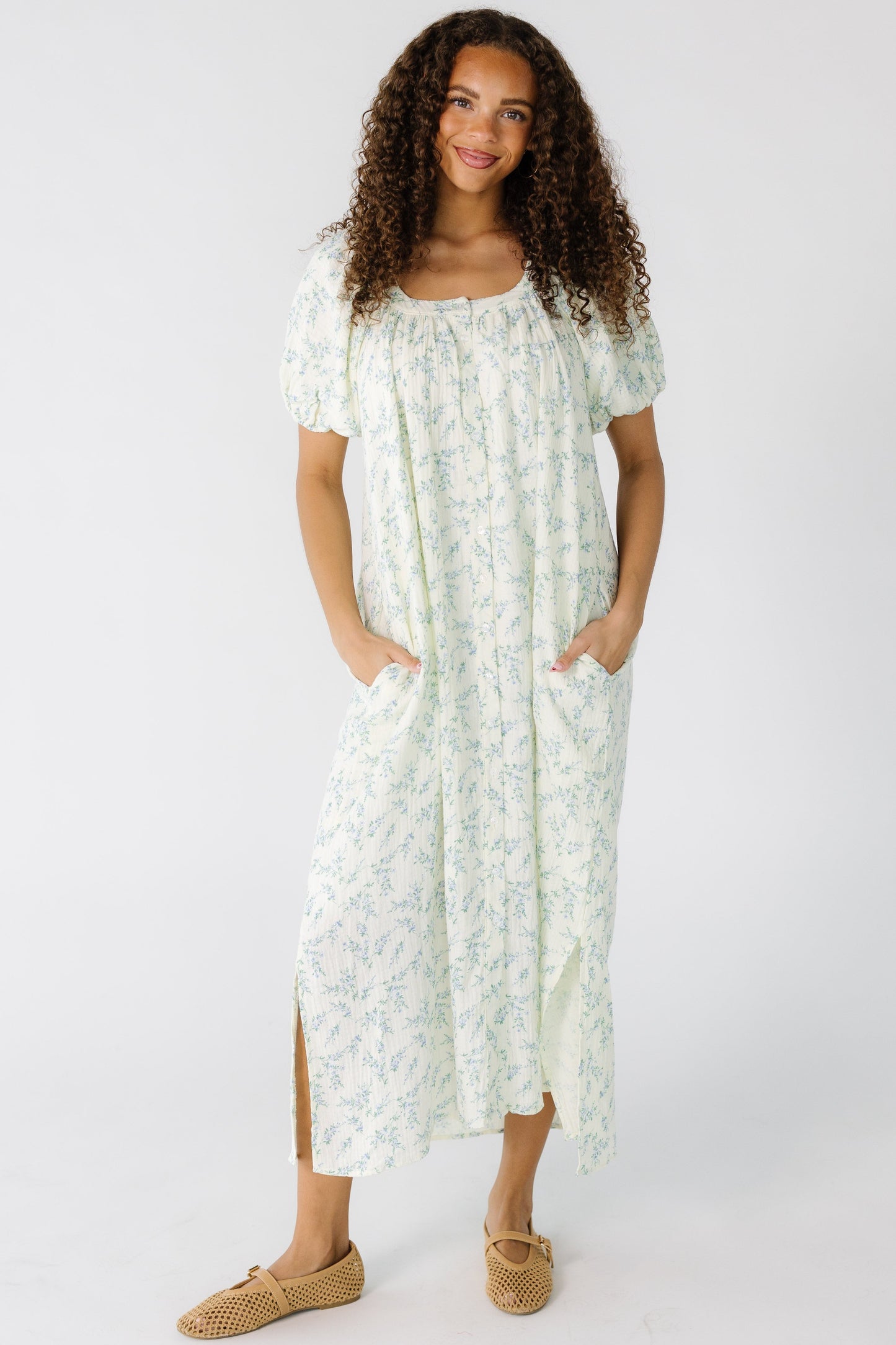 Teen girl wearing a modest cream and blue floral button down midi dress with short puff sleeves and a scoop neckline.