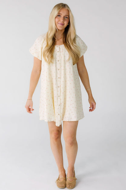 Woman wearing a cream mini dress with a pink bow print with a round neckline and short balloon sleeves.