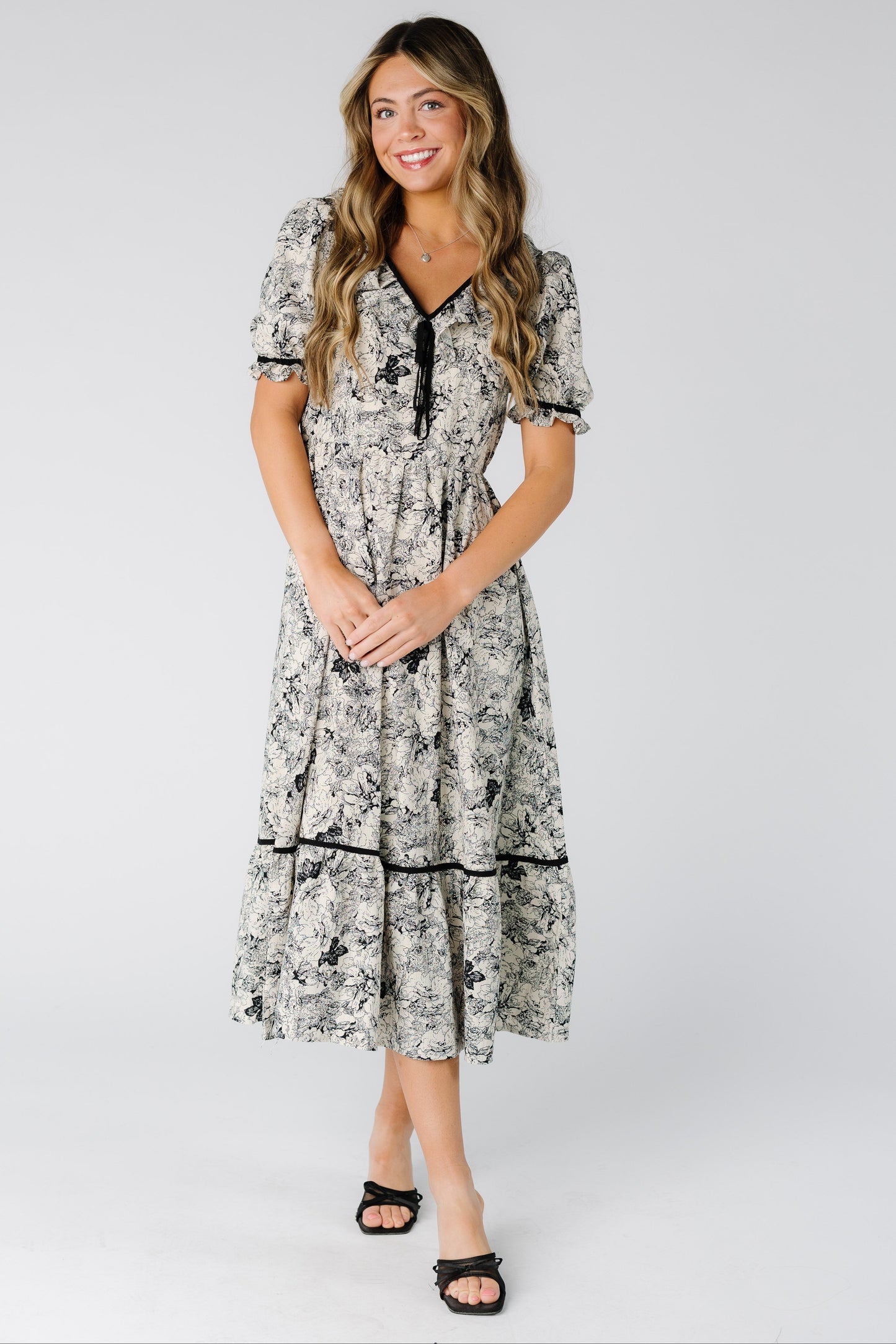 Woman wearing a  modest black and white print midi dress with a V-neckline and short puff sleeves