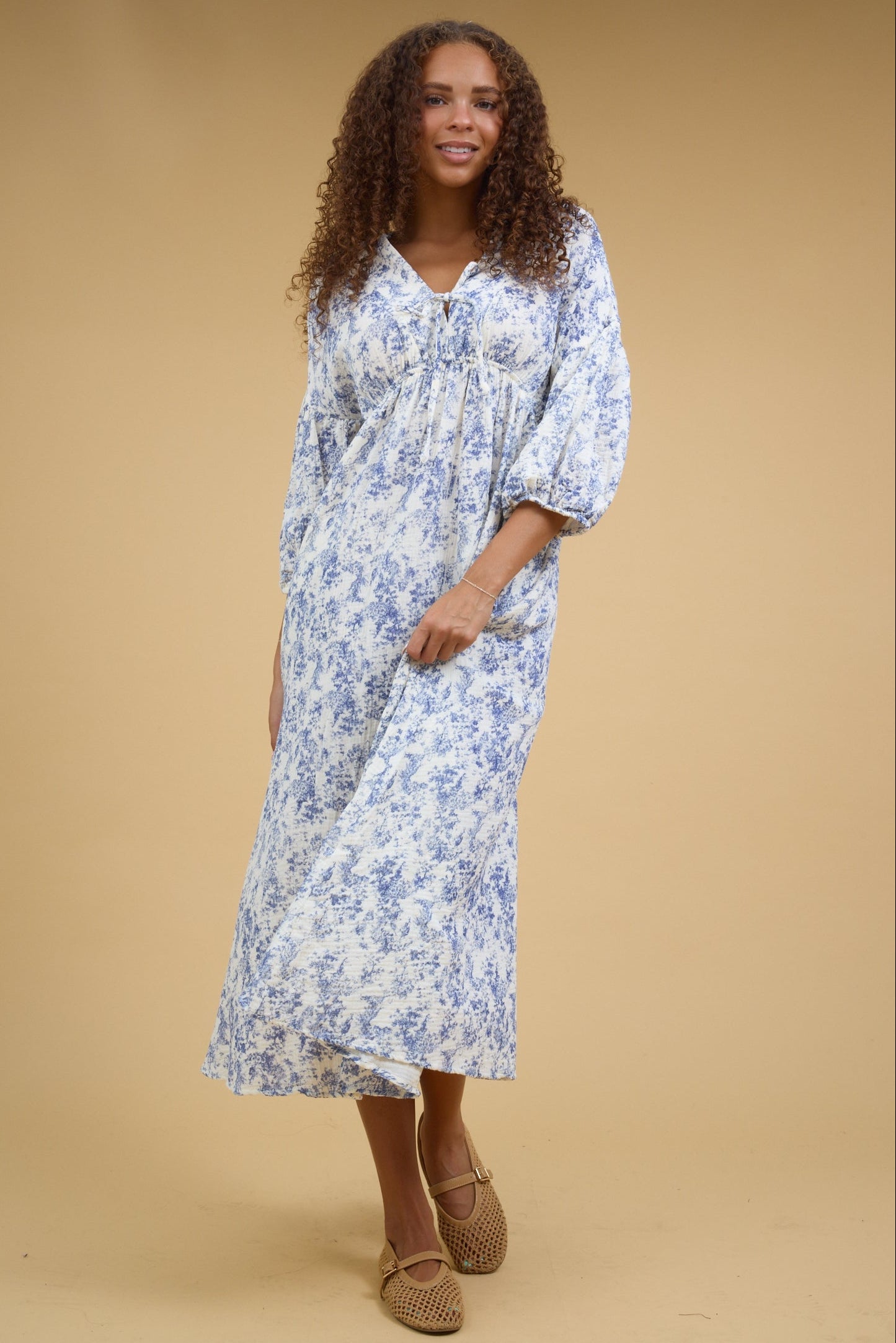 Young woman wearing a modest white & blue print midi dress with half length sleeves, empire waist and a V-neckline.