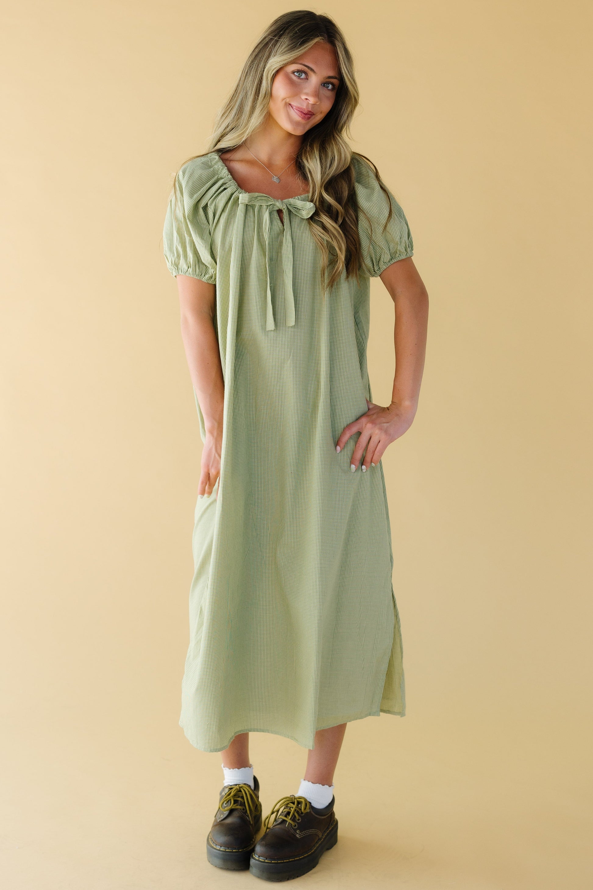 Young woman wearing a modest green gingham midi dress with a drawstring square neckline and large puff sleeves.