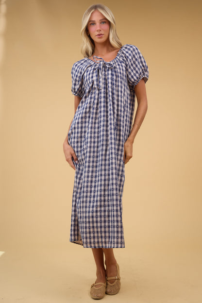 Young woman wearing a modest, loose fitting blue gingahm midi dress with a drawstring neckline and short balloon sleeves.