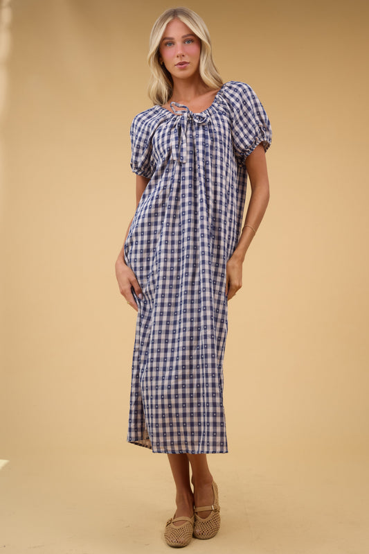 Young woman wearing a modest, loose fitting blue gingahm midi dress with a drawstring neckline and short balloon sleeves.