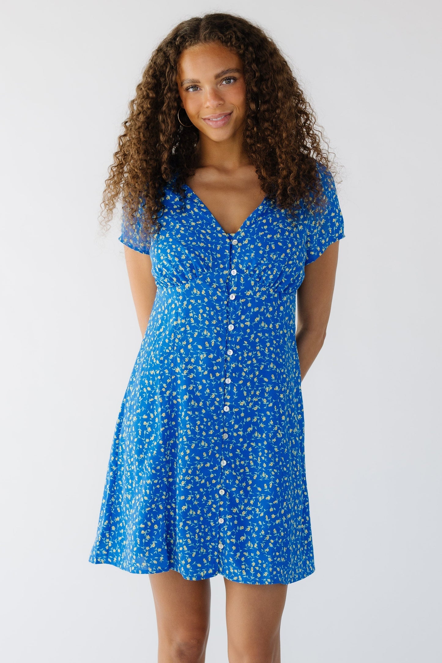 Young woman wearing a modest blue floral knee dress that buttons down the front with a V-neckline and short sleeves.