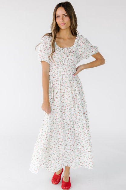 Woman wearing an ivory and red floral print midi-maxi dress with a full skirt, snug waist and closer fitting bodice.
