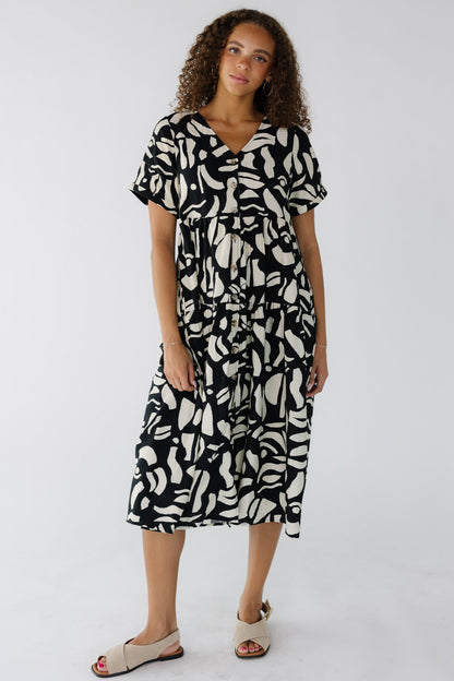 Teen girl wearing a modest cream and black abstract print button down midi dress wtih a V-neckline and short sleeves.