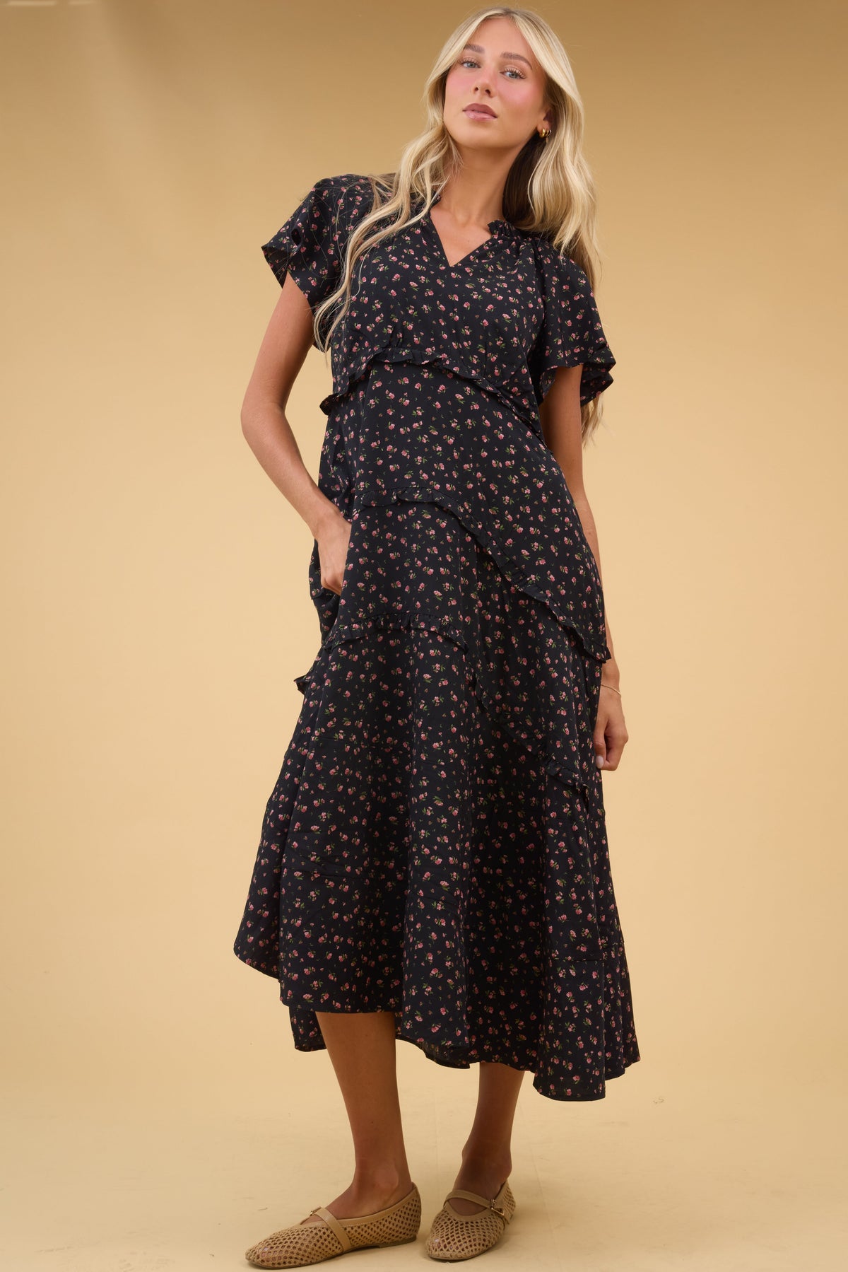Young woman wearing a black floral midi-maxi dress with a V-neckline, short flutter sleeves and a tiered skrit with narrow ruffles.
