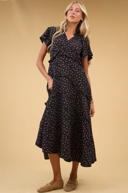 Young woman wearing a black floral midi-maxi dress with a V-neckline, short flutter sleeves and a tiered skrit with narrow ruffles.