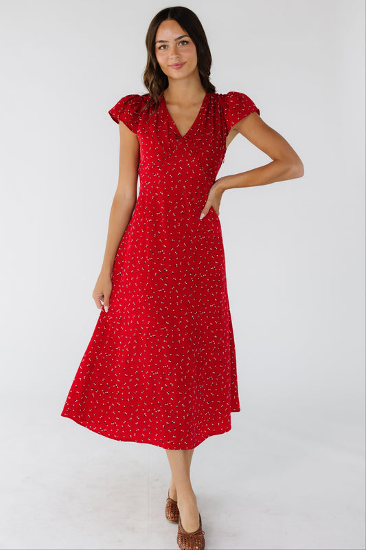 Young woman wearing a red floral midi dress with a V-neckline, short flutter sleeves and a pointed empire waist.