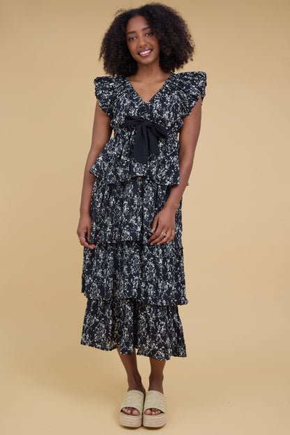 Young woman wearing a modest black floral midi dress with multiple layered tiers, V-neckline and gathered cap sleeves.