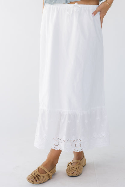 Woman wearing a white A-line midi skirt with a wide eyelet bottom ruffle with a narrow elastic waist.