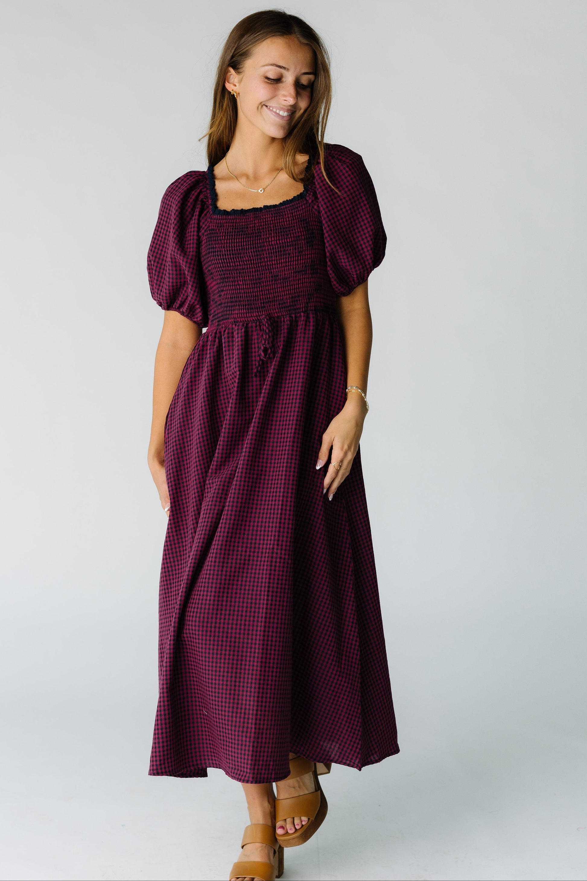 Woman wearing a burgundy gingham midi dress with a square neckline, short balloon sleeves and full skirt.