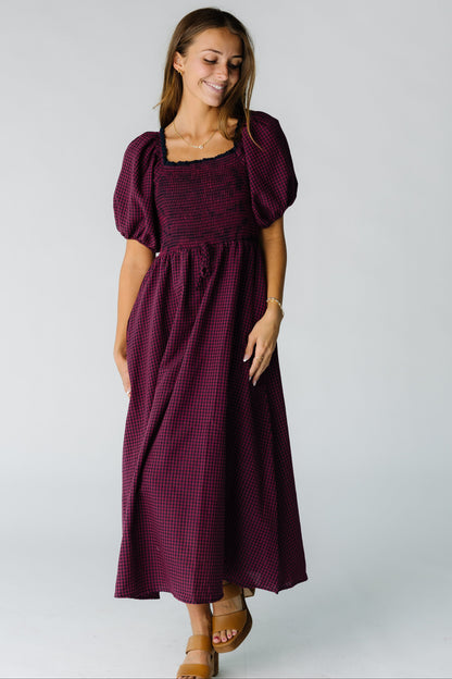 Woman wearing a burgundy gingham midi dress with a square neckline, short balloon sleeves and full skirt.
