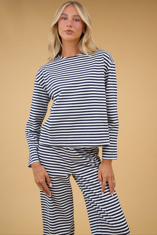 A young woman wairng a navy & white stripe lounge set with long sleeves and wide leg lounge pants.