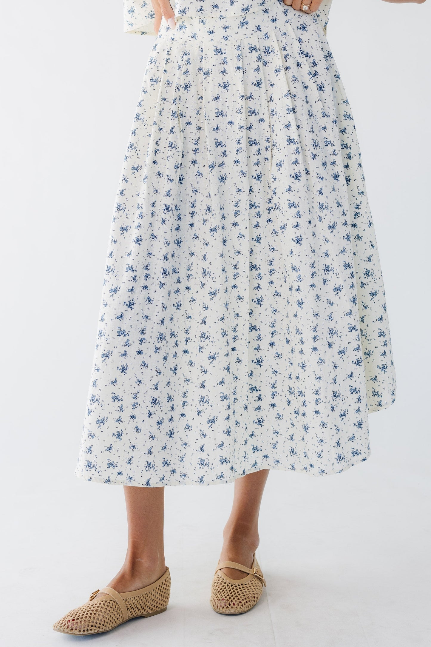 Young woman wearing a modest cream & blue floral print midi skirt with pleat details.