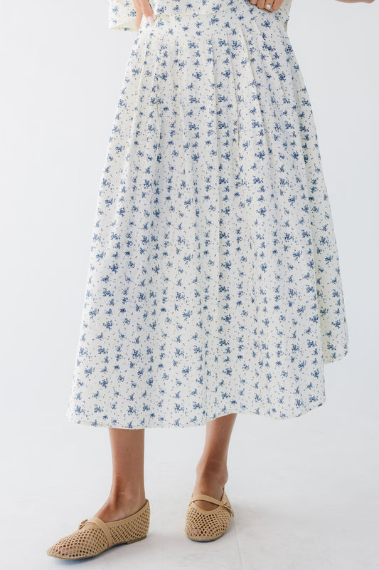 Young woman wearing a modest cream & blue floral print midi skirt with pleat details.