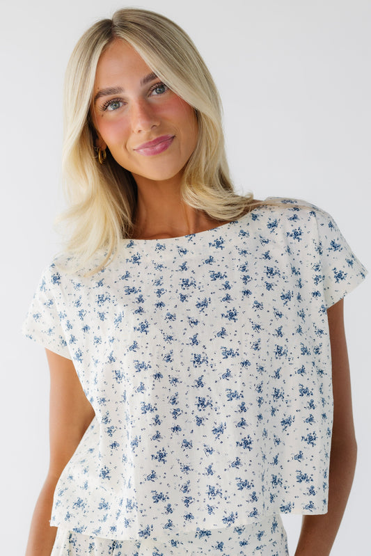 Young woman wearing a modest cream and blue floral print top with short sleeves and a round neckline.