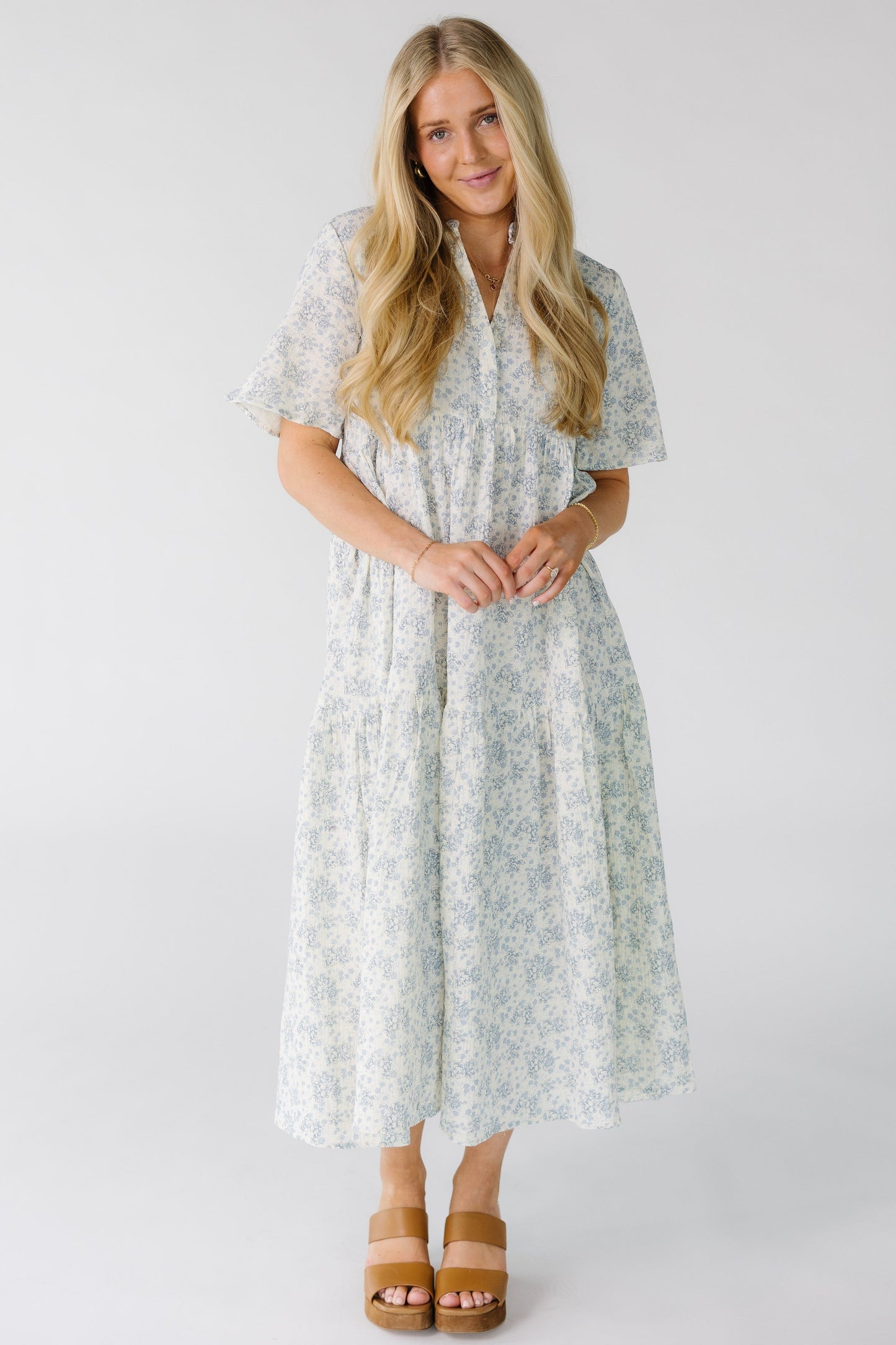 Woman wearing a white floral print midi dress with a V-neckline and short sleeves with an empire waist.
